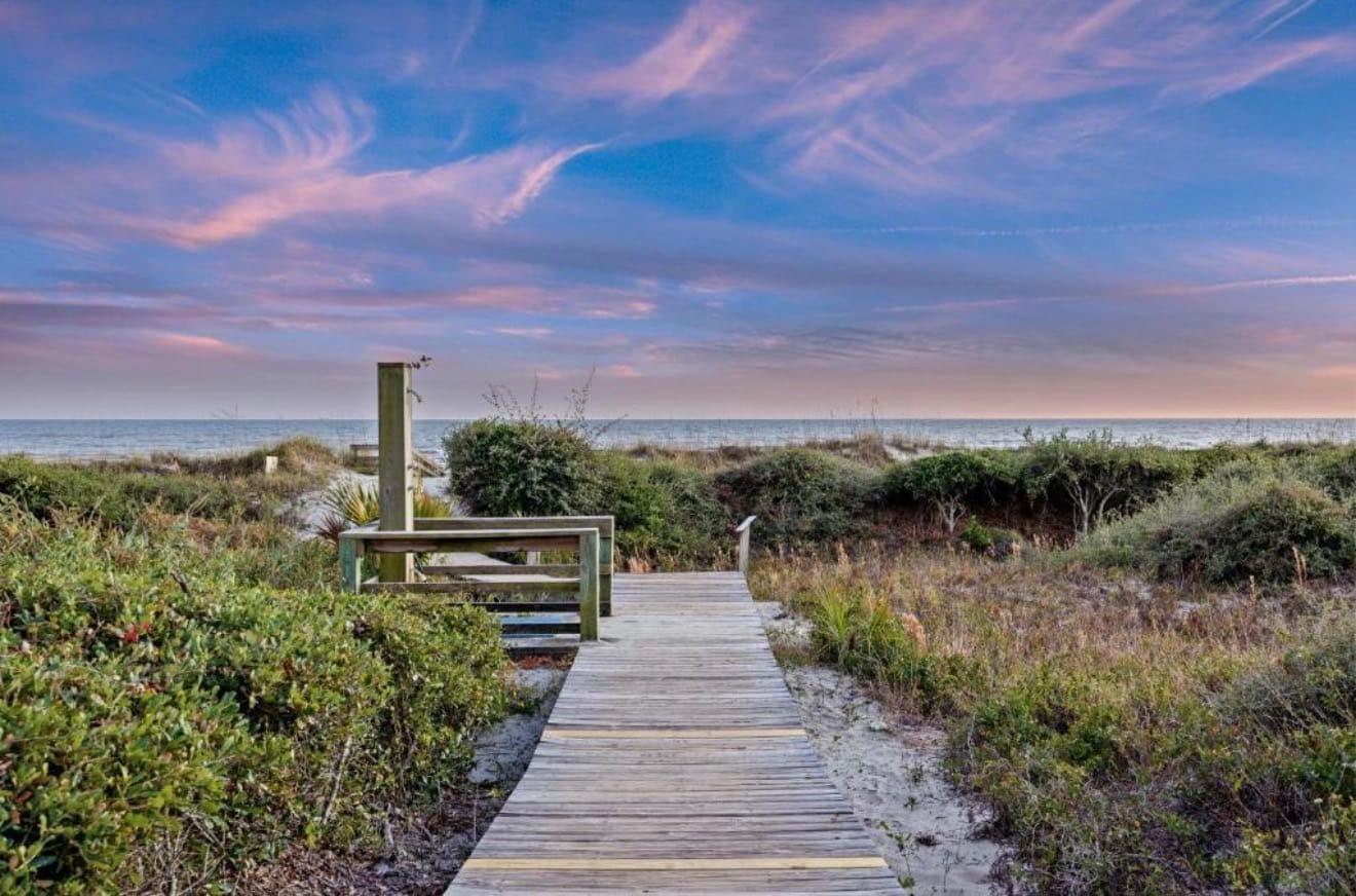 Wooden boardwalk with an outdoor shower post crossing the dunes to the ocean at dusk